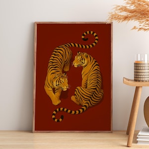 May include: A rectangular wall art print in a wooden frame featuring two tigers with orange fur and black stripes on a solid dark red background. One tiger is depicted in a walking pose while the other is sitting, both facing each other.
