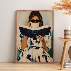 May include: A framed art print depicts a person reading a book while holding a cup of coffee. The person is wearing sunglasses and a white dress with blue floral patterns. The artwork has a soft, painterly style with a neutral color palette.