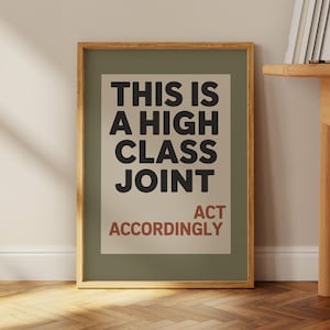May include: A framed art print with the text "THIS IS A HIGH CLASS JOINT" in black, and "ACT ACCORDINGLY" in red. The print is set against a light green background, framed in a natural wood tone.