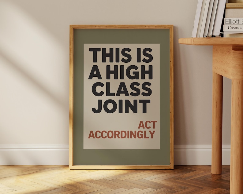 May include: A framed art print with the text "THIS IS A HIGH CLASS JOINT" in black, and "ACT ACCORDINGLY" in red. The print is set against a light green background, framed in a natural wood tone.