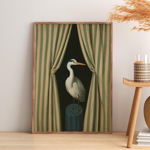 May include: Framed art print featuring a heron standing on a blue pedestal against a dark backdrop. The artwork is framed with a wooden border and includes green and beige striped curtains on either side. The heron has a long neck and orange beak.