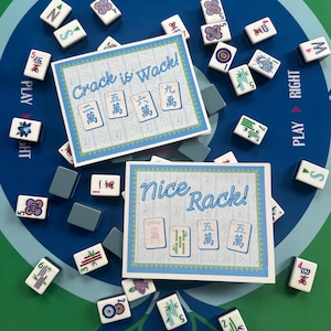May include: A colorful Mahjong game set with tiles and cards. The cards read "Crack is Wack!" and "Nice Rack!". The tiles are white with black and red symbols. The game is set on a blue and green game board.