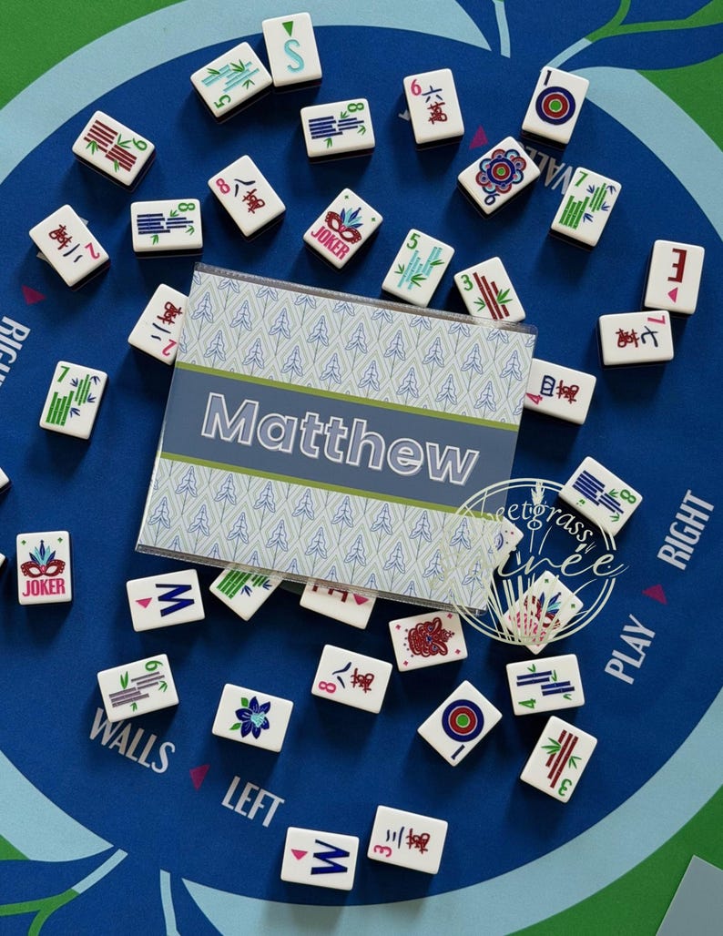 May include: A blue Mahjong game mat with scattered tiles. A personalized card with the name "Matthew" is in the center. The tiles are white with various symbols and numbers. The mat has text that says "Walls", "Left", "Play", and "Right".