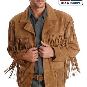 Puede incluir: Chaqueta de ante marrón con flecos. La chaqueta tiene una botonadura frontal, un cuello y un cinturón. La imagen también incluye el texto "DELIVERED DUTY PAID" y "USA & EUROPE" con las banderas estadounidense y europea.
