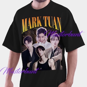 May include: Black t-shirt featuring a graphic of four people and the text "MARK TUAN" in yellow. The graphic has a vintage aesthetic. The shirt is a crew neck and appears to be made of cotton.