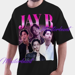 Puede incluir: Camiseta negra con un gráfico de cuatro personas y el nombre "JAY B" en rosa. El diseño tiene una estética vintage, sobre un fondo degradado púrpura y rosa.