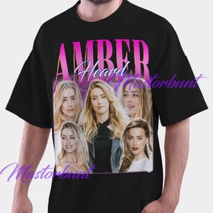 Op de afbeelding: Zwart T-shirt met een collage van vijf afbeeldingen van een vrouw met blond haar. Het woord "AMBER" is gedrukt in een roze en paarse gradiëntlettertype boven het woord "Heard" in een cursief lettertype.