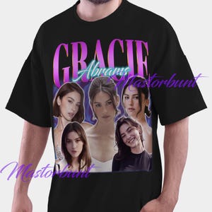 Op de afbeelding: Zwart T-shirt met een afbeelding van Gracie Abrams en haar naam in een paarse en blauwe gradiëntkleur. De afbeelding bevat meerdere afbeeldingen van Gracie Abrams. Het T-shirt heeft een casual stijl.