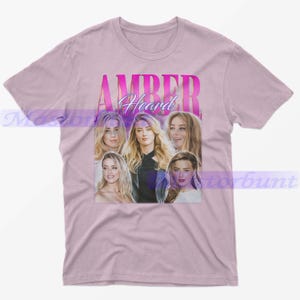 May include: A light pink t-shirt featuring a graphic of Amber Heard. The graphic includes the name "AMBER Heard" in a pink gradient font, with multiple images of the actress. The shirt is made of a soft material.