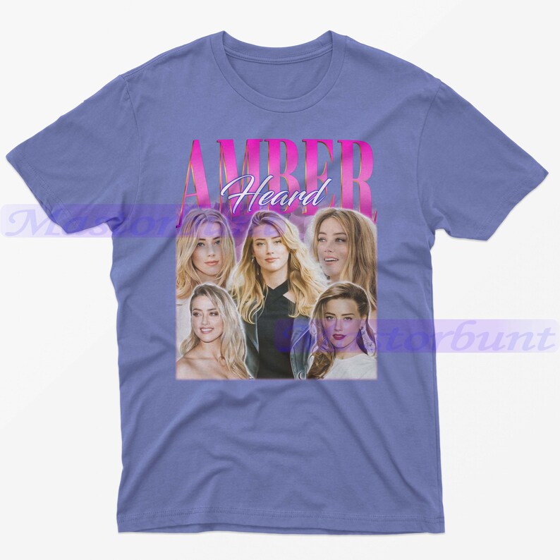 May include: A light blue t-shirt featuring a collage of images of Amber Heard, with the name "AMBER Heard" in pink text. The shirt is a crew neck style.