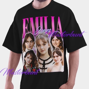 May include: Black t-shirt featuring a graphic of Emilia Jones with the name "Emilia Jones" in pink and white text. The graphic includes multiple images of the actress. The shirt is a crew neck style.