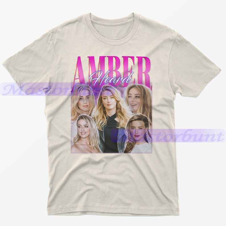 May include: Cream-colored t-shirt featuring a graphic of Amber Heard. The design includes multiple images of the actress with the name "AMBER Heard" in a pink and purple gradient font. The shirt is made of a soft material.