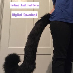Op de afbeelding: Een zwarte nep-bontstaart met een gekrulde punt. De staart wordt vastgehouden door een persoon die een zwarte broek en een blauw shirt draagt. De tekst "Feline Tail Pattern" en "Digital Download" is zichtbaar in de afbeelding.