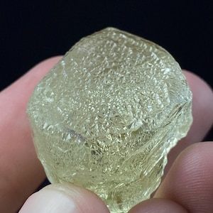 Op de afbeelding: Een grote, doorschijnende, lichtgroene kristal met een ruw, gefacetteerd oppervlak. De kristal heeft een unieke, geometrische vorm en is een prachtig voorbeeld van natuurlijke schoonheid.