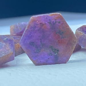 May include: Four purple and red gemstone crystals with a hexagonal shape. The crystals have a rough, natural texture.