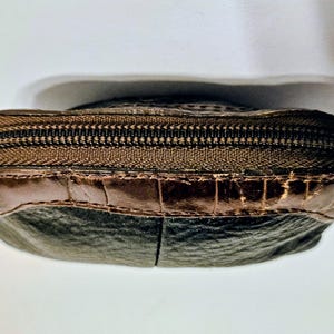 May include: A small, brown leather coin purse with a zipper closure. The purse has a dark brown zipper and a lighter brown leather accent at the top. The bottom portion of the purse is a darker shade of brown.