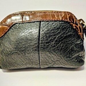 May include: A small, textured coin purse with a brown, crocodile-embossed top and a black, leather-like body. The purse has a zipper closure with a brown pull tab. The overall shape is rounded and compact.