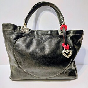 Puede incluir: Bolso tote de cuero negro con un dise&ntilde;o en forma de coraz&oacute;n cosido en la parte delantera. El bolso presenta fijaciones de asa de metal plateado y un charm de coraz&oacute;n rojo y plateado. El bolso tiene un asa superior.