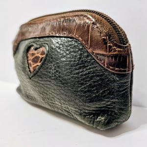 May include: A small, black leather coin purse with a brown, textured top and a heart-shaped cutout revealing a brown, patterned interior. The purse has a zipper closure.
