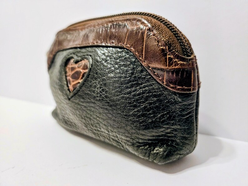 May include: A small, black leather coin purse with a brown, textured top and a heart-shaped cutout revealing a brown, patterned interior. The purse has a zipper closure.