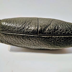 May include: A black leather clutch with a textured surface. The clutch is rectangular with rounded edges and a visible seam down the middle. The leather has a slightly metallic sheen.
