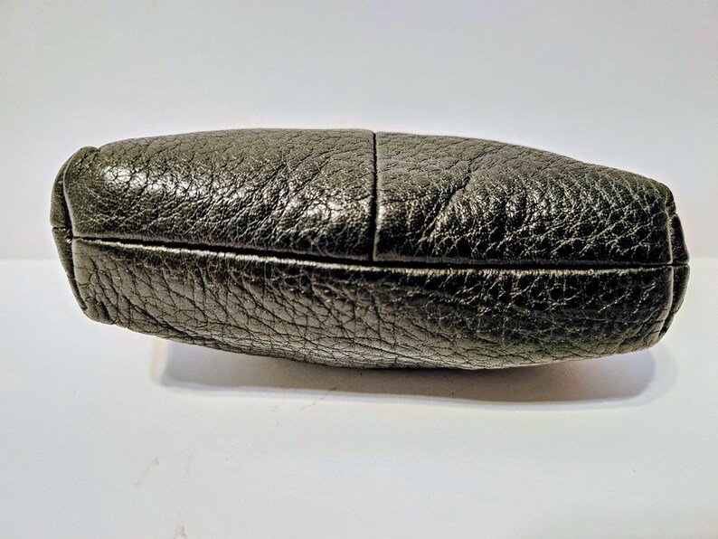 May include: A black leather clutch with a textured surface. The clutch is rectangular with rounded edges and a visible seam down the middle. The leather has a slightly metallic sheen.