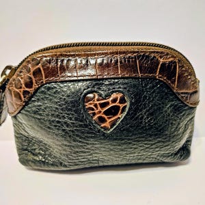 May include: A small, black leather coin purse with a brown, crocodile-textured top and a heart-shaped accent. The purse has a zipper closure and a small pull tab. The heart accent is also textured.