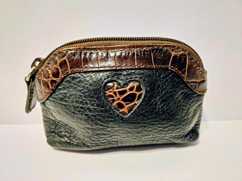 May include: A small, black leather coin purse with a brown, crocodile-textured top and a heart-shaped accent. The purse has a zipper closure and a small pull tab. The heart accent is also textured.