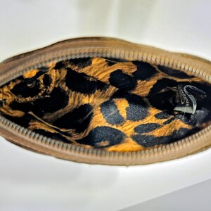May include: A small, open, brown zippered pouch with a gold zipper pull. The interior features a leopard print pattern in black and gold. The pouch is likely made of leather or a similar material.