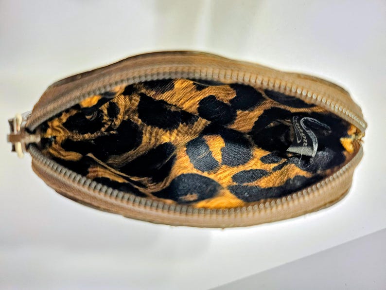 May include: A small, open, brown zippered pouch with a gold zipper pull. The interior features a leopard print pattern in black and gold. The pouch is likely made of leather or a similar material.