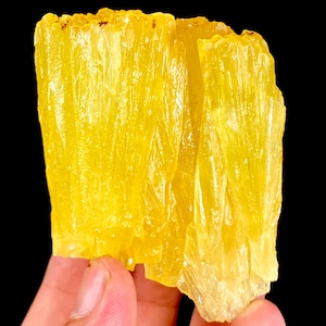 Puede incluir: Un espécimen mineral de color amarillo brillante que presenta un grupo de formaciones cristalinas verticales, translúcidas y con una textura fibrosa y estriada. La estructura muestra bordes afilados y dentados con un tono amarillo dorado uniforme.