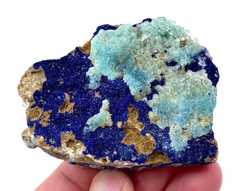 May include: A close-up of a blue and green mineral specimen. The specimen has a rough, textured surface and is covered in small crystals. The blue crystals are clustered together, while the green crystals are more spread out.