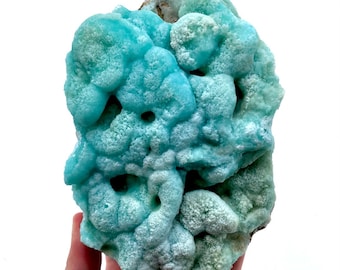 May include: A large, blue and green, naturally formed, mineral specimen with a rough, textured surface. The mineral has a unique, organic shape with many holes and crevices.