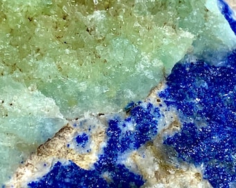 May include: A close-up of a green and blue mineral specimen. The green mineral is a cluster of small crystals, while the blue mineral is a layer of smaller crystals. The two minerals are joined together by a layer of white rock.