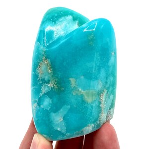 May include: A smooth, polished turquoise blue gemstone with white and green inclusions. The gemstone is shaped like a heart and has a natural, organic look.