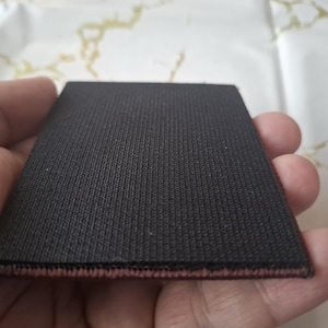 K&ouml;nnte beinhalten: Ein rechteckiger, schwarzer Stoffflicken mit strukturierter Oberfl&auml;che. Der Flicken hat einen d&uuml;nnen, r&ouml;tlich-rosa Rand. Der Artikel wird in der Hand einer Person gehalten.