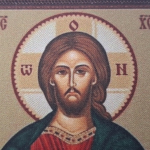 K&ouml;nnte beinhalten: Ikone, die eine Figur mit braunem Haar und Bart zeigt, die ein rotes und gr&uuml;nes Gewand tr&auml;gt. Die Figur ist von einem Heiligenschein mit Text in einem kreisf&ouml;rmigen Muster umgeben. Der Hintergrund ist hellbeige.