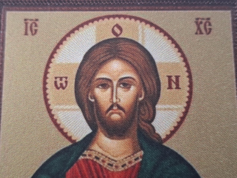 K&ouml;nnte beinhalten: Ikone, die eine Figur mit braunem Haar und Bart zeigt, die ein rotes und gr&uuml;nes Gewand tr&auml;gt. Die Figur ist von einem Heiligenschein mit Text in einem kreisf&ouml;rmigen Muster umgeben. Der Hintergrund ist hellbeige.