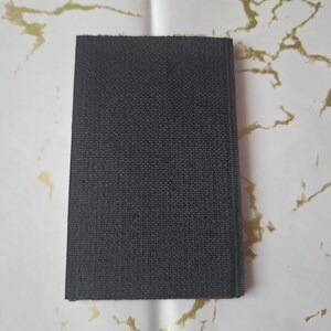 May include: A rectangular, dark gray fabric swatch with a textured surface. The swatch is displayed against a white background with gold-colored marbling.