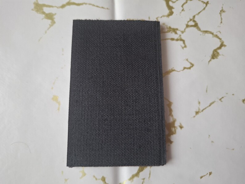 May include: A rectangular, dark gray fabric swatch with a textured surface. The swatch is displayed against a white background with gold-colored marbling.
