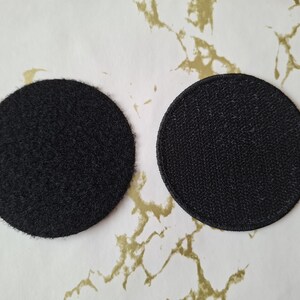 Op de afbeelding: Twee ronde zwarte patches, een met een pluche textuur en de andere met een gladde textuur.