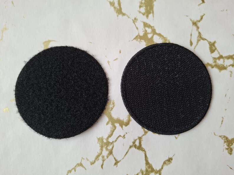Op de afbeelding: Twee ronde zwarte patches, een met een pluche textuur en de andere met een gladde textuur.