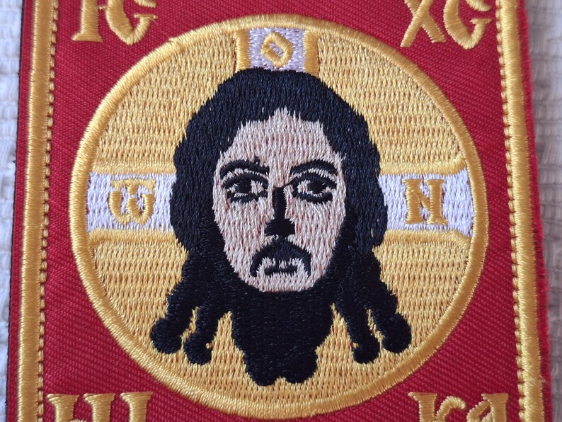 Op de afbeelding: Geborduurde patch met een gedetailleerde afbeelding van een religieuze figuur met donker haar en een baard, geplaatst in een gouden cirkel. Het ontwerp staat op een rode achtergrond met gouden letters en rand, geschikt voor religieuze kleding of ambachten.