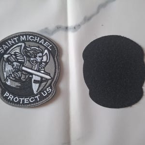 May include: Embroidered patch depicting Saint Michael with a sword and shield, with the text "SAINT MICHAEL PROTECT US" in a circular design. A separate black felt patch is also visible.