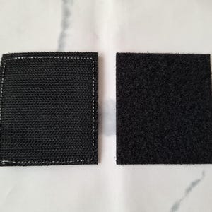 May include: Two black square hook and loop fastener patches. One patch has a woven texture with white stitching around the edges. The other patch has a fuzzy texture.