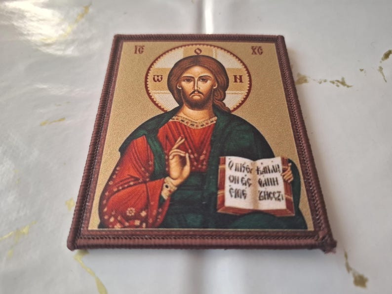 K&ouml;nnte beinhalten: Rechteckige religi&ouml;se Ikone mit einer Darstellung von Jesus Christus. Das Bild zeigt Jesus mit Heiligenschein, der ein Buch h&auml;lt und ein rotes Gewand und einen gr&uuml;nen Umhang tr&auml;gt. Die Ikone hat einen braunen Rand.
