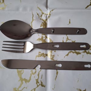 以下が含まれることがあります： スプーン、フォーク、ナイフを含むステンレス製のカトラリーセット。各カトラリーは、鍵穴型の切り欠きが付いた長いハンドルが付いています。ナイフは鋸歯状のエッジと栓抜きが付いています。