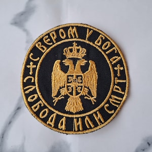 Puede incluir: Un parche bordado negro con un águila dorada y el texto "СВЕРOМ У БОГА + СЛОБОДА ИЛИ СМРТ +" en escritura cirílica.