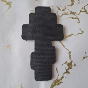 Pu&ograve; includere: Un oggetto nero, strutturato, a forma di croce. L'oggetto ha una serie di estensioni rettangolari. Lo sfondo &egrave; una superficie bianca con marmorizzazione dorata.