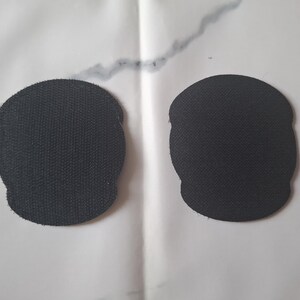 May include: Two black, skull-shaped patches with a textured surface are displayed against a white background. The patches are identical in shape and size, with a slightly rounded top and a scalloped bottom.